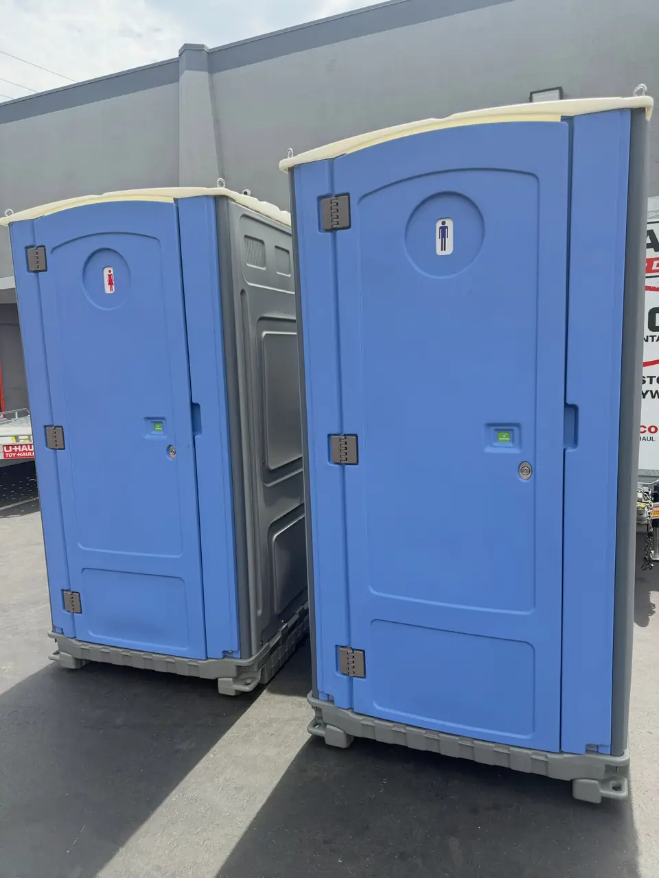 Two clean blue standard porta potties set side by side on level pavement